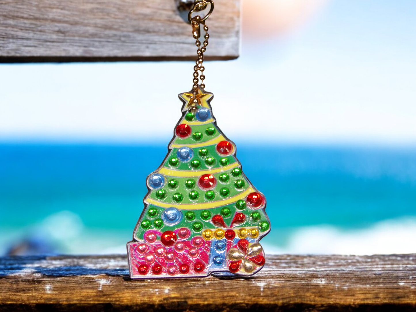 Christmas tree keychain with colorful presents hanging on wooden surface near ocean background