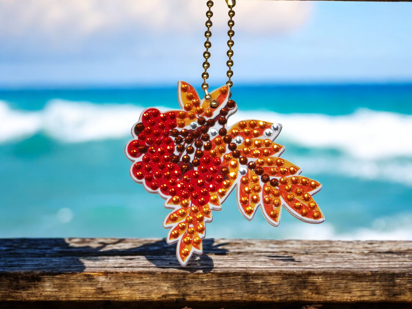 Colorful maple leaf keychain with red and orange rhinestones hanging by the ocean