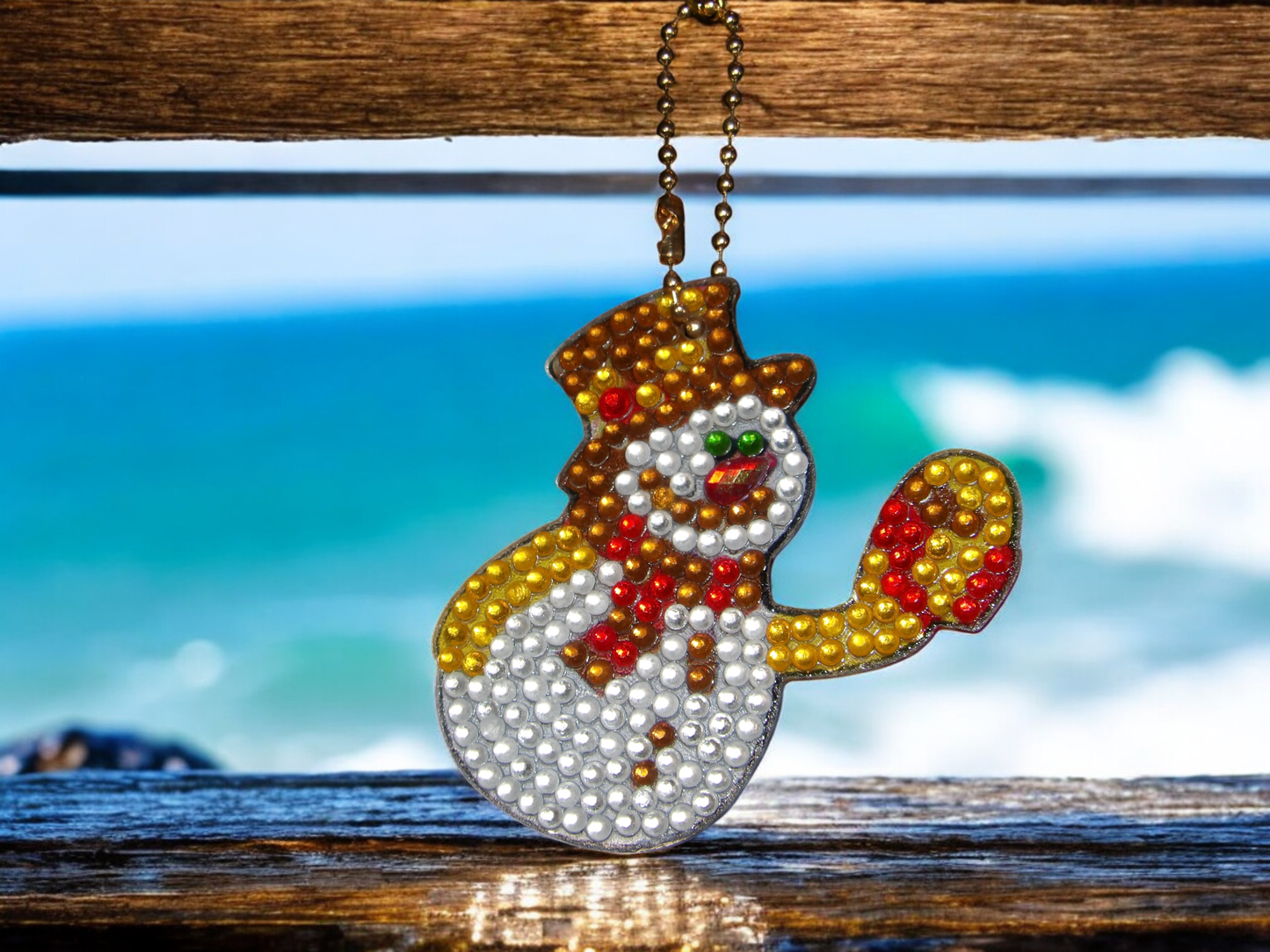 Golden snowman keychain hanging on a wooden surface with ocean background