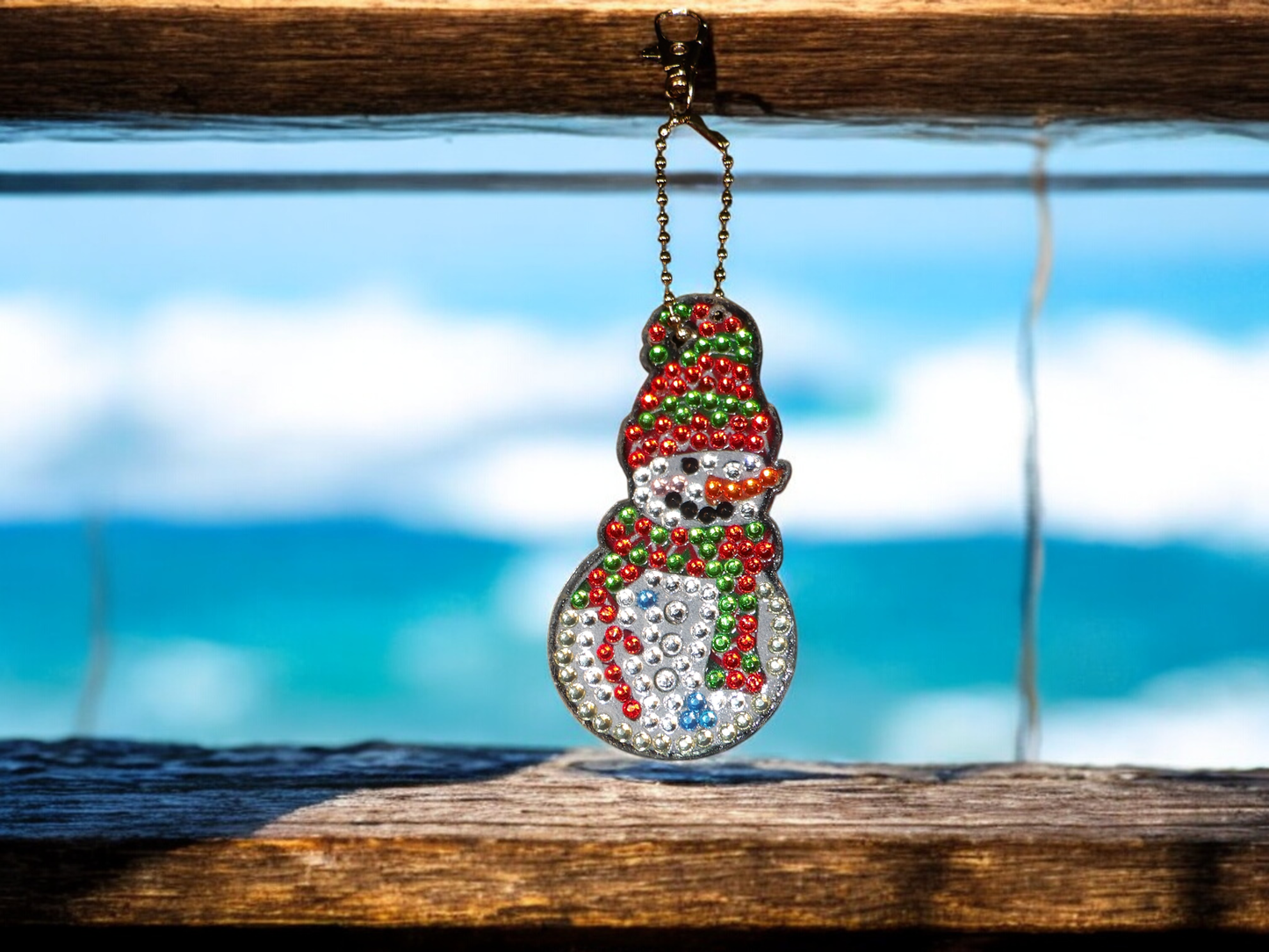 Red and green hat and scarf snowman keychain hanging on a chain with ocean background