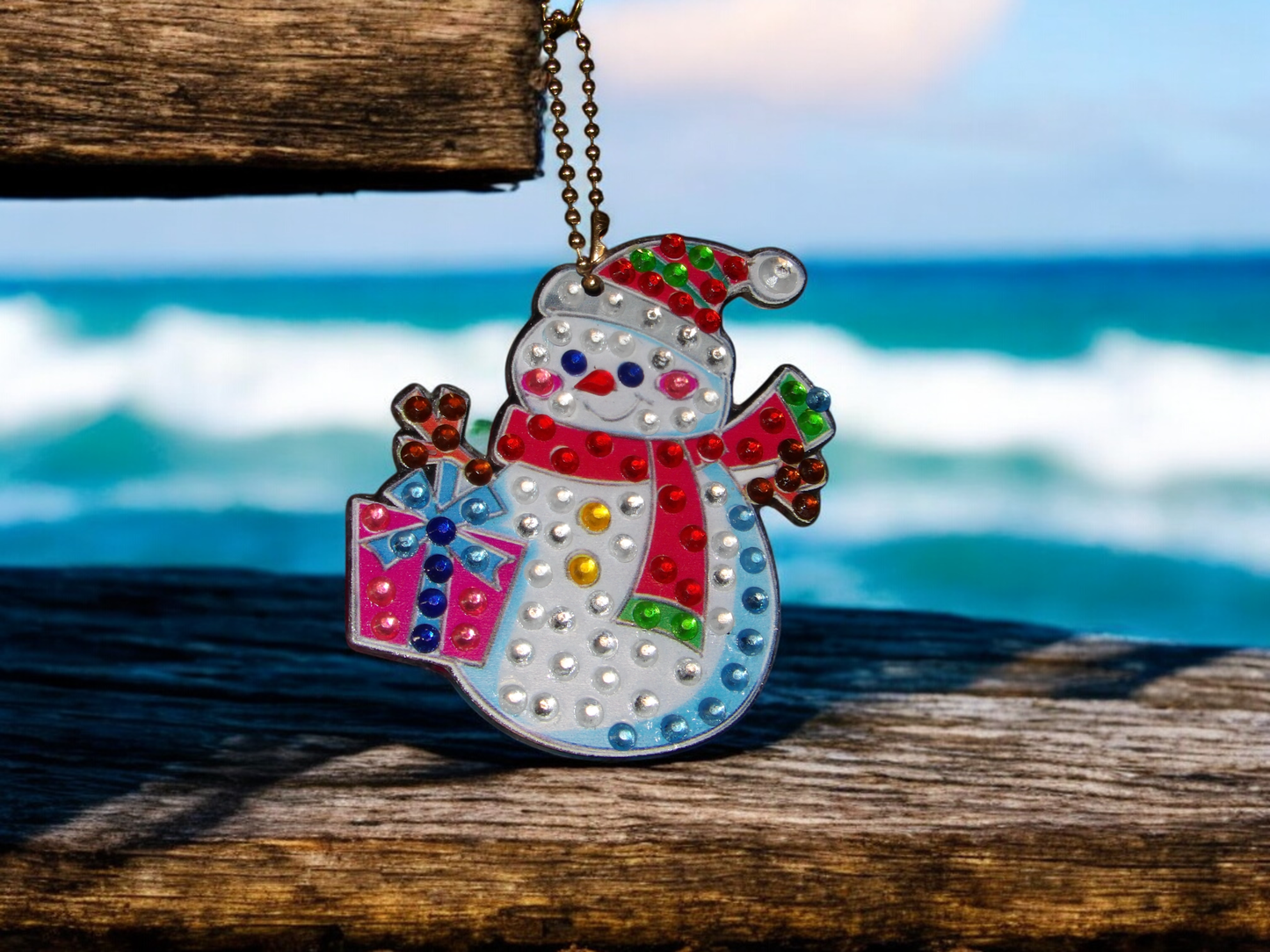 Present Snowman Keychain hanging on wooden surface with ocean background