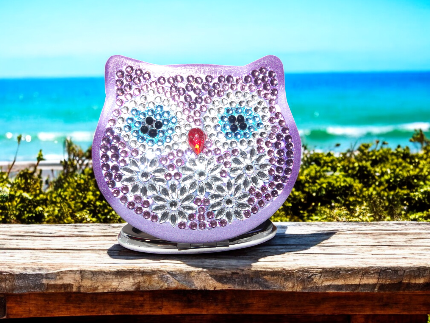 Purple Owl Face Pocket Mirror with magnification and decorative gems on a beach background