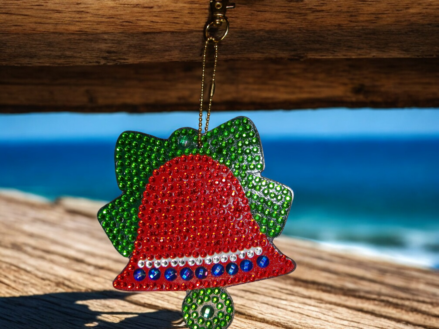 Red Bell Keychain decorated with colorful rhinestones hanging on a wooden surface with ocean background