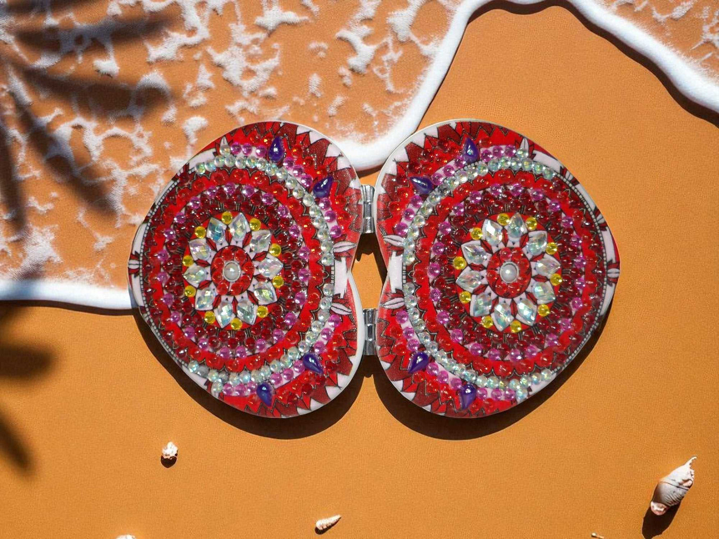 Red and pearl heart shape pocket mirror with mandala design and magnification feature opened on an orange surface
