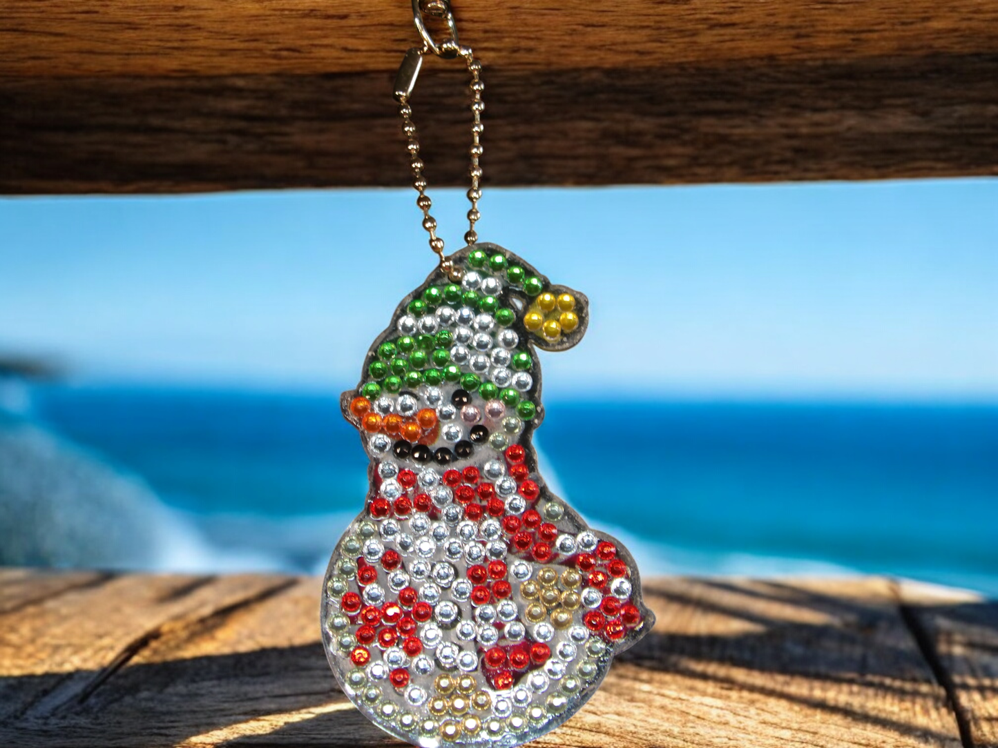 Red Gold Green snowman keychain hanging with ocean background