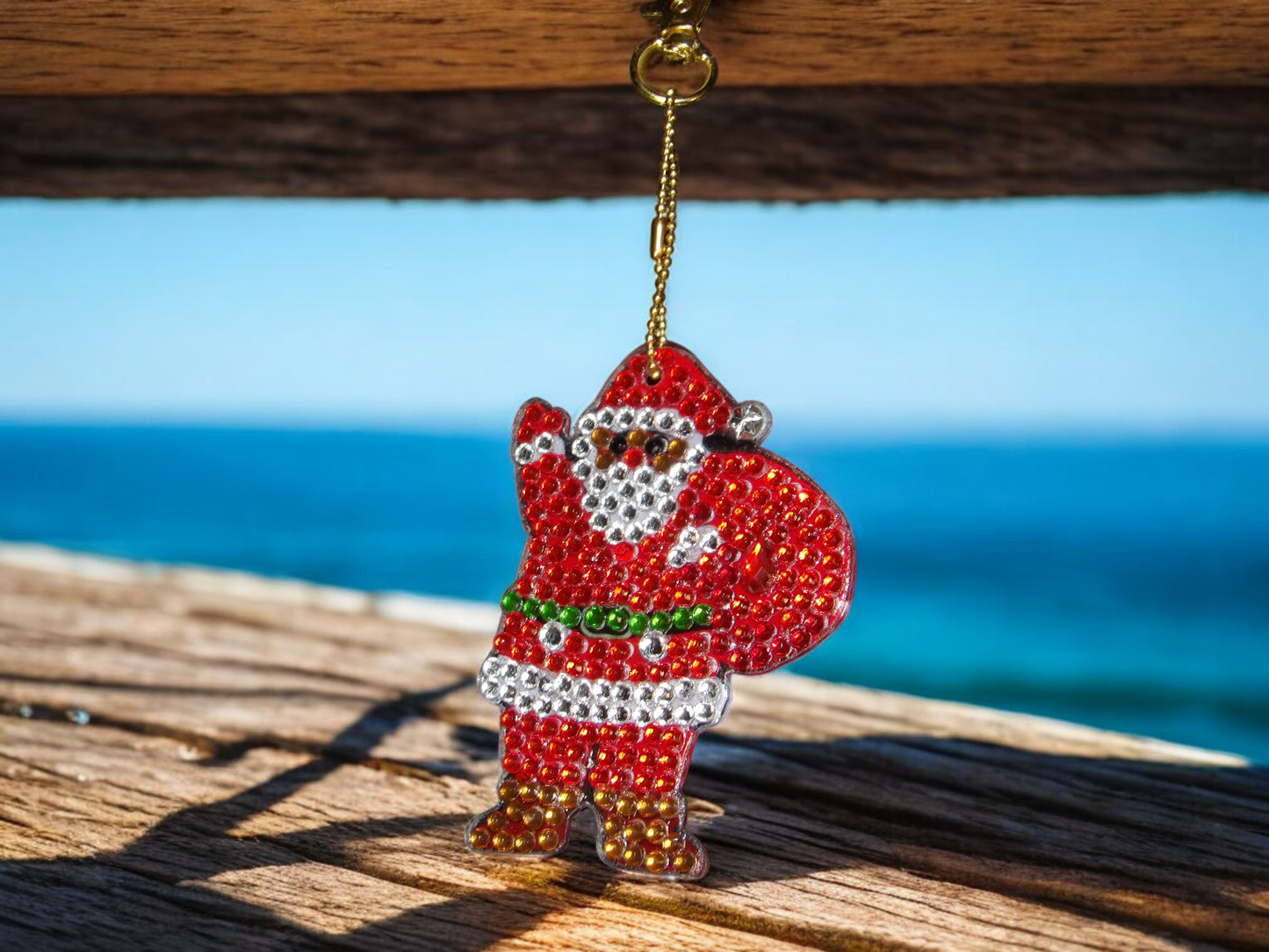 Santa Clause keychain decorated with sparkling rhinestones hanging on a golden chain against a wooden background and ocean view