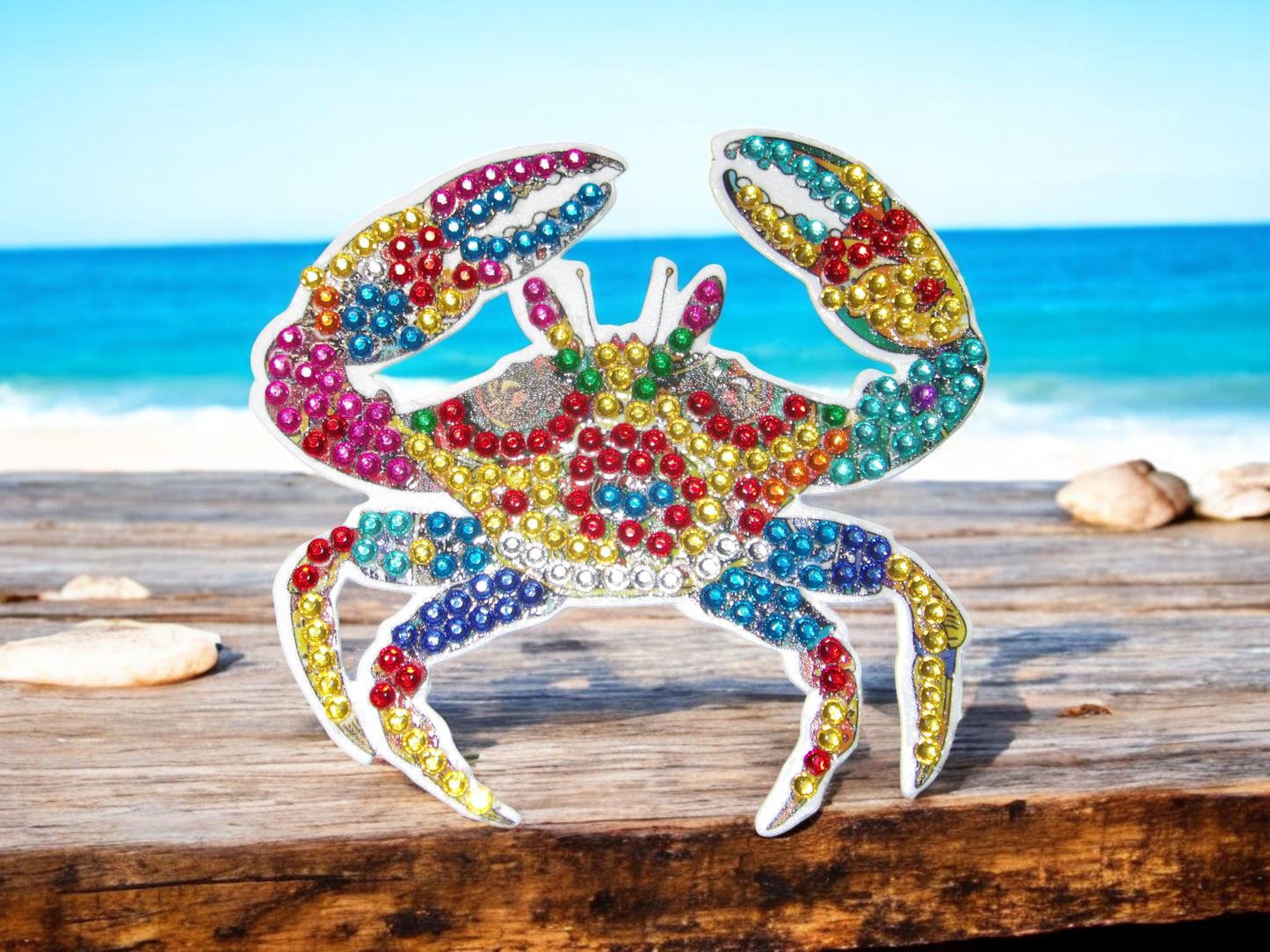 Colorful crab-shaped magnet decorated with multicolored rhinestones on wooden surface by the sea