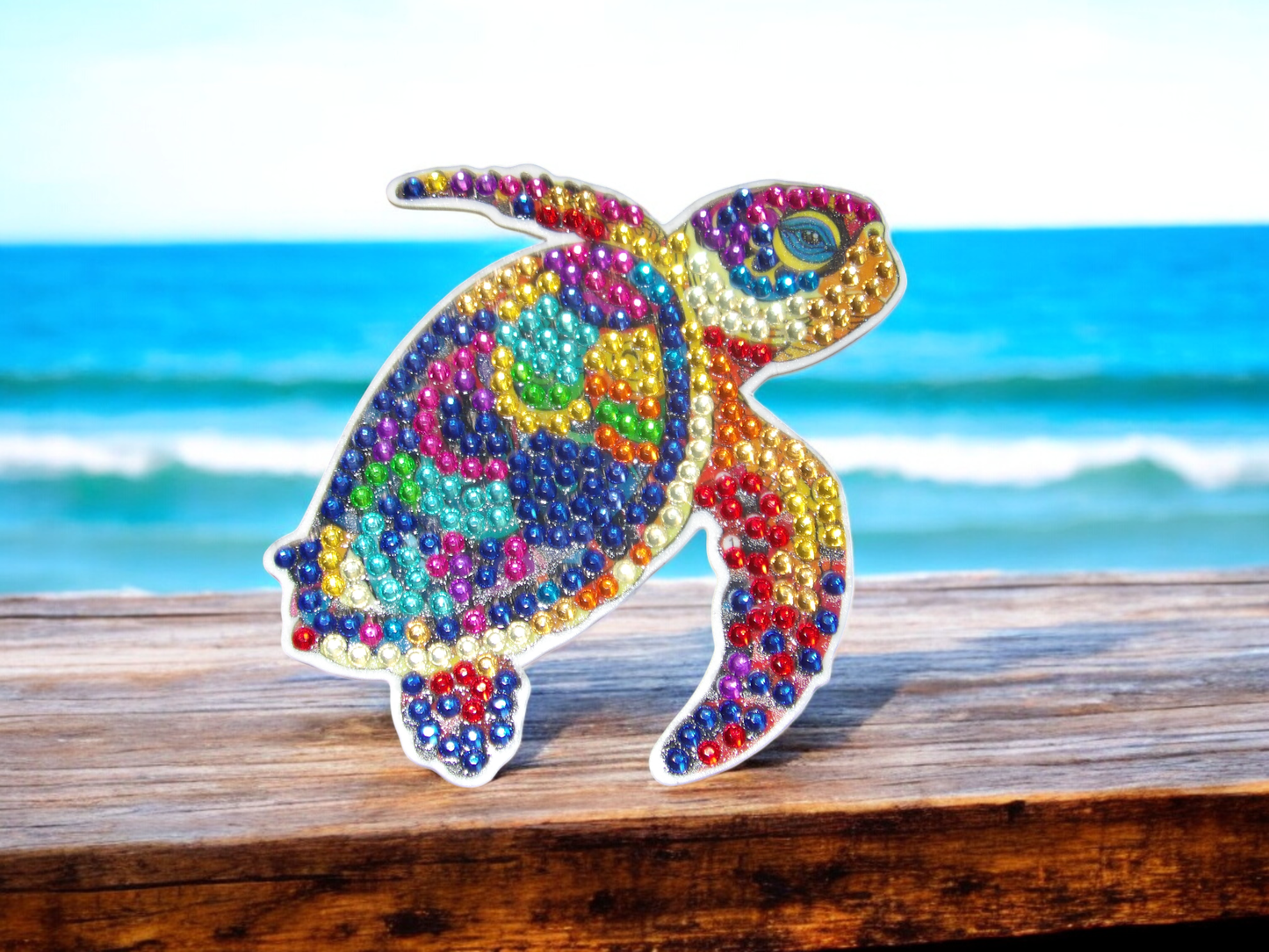 Colorful lively turtle magnet decorated with vibrant beads on wooden surface by the beach ocean background