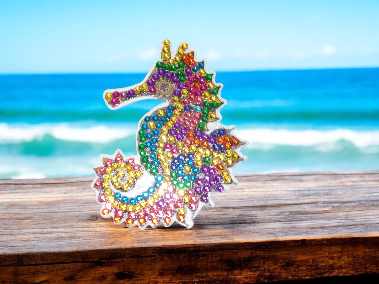 Colorful seahorse magnet decorated with multicolored beads on wooden surface by the ocean