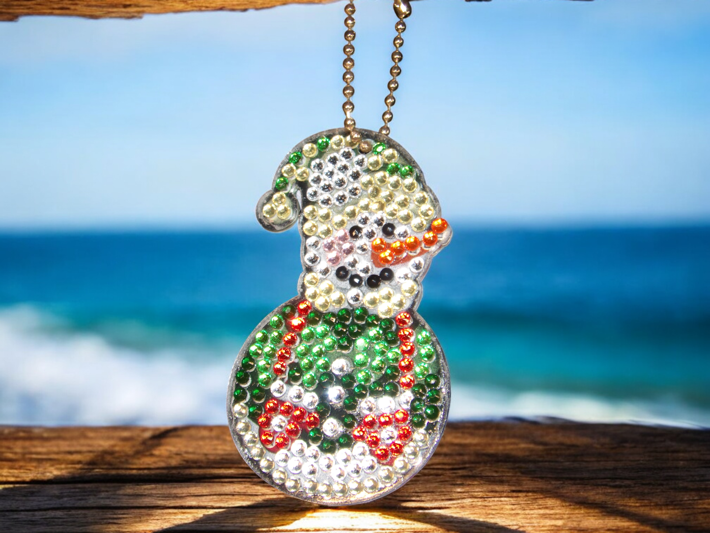 Stripped Hat Snowman Keychain with colorful beads hanging on wooden surface with ocean background