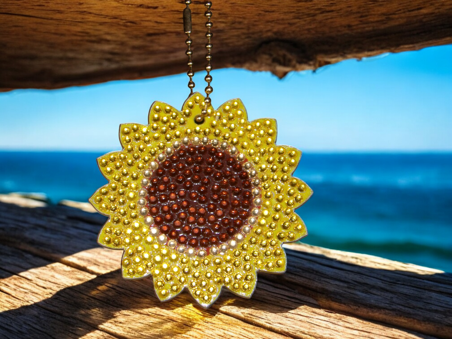 Sunflower keychain hanging on wooden surface with ocean background