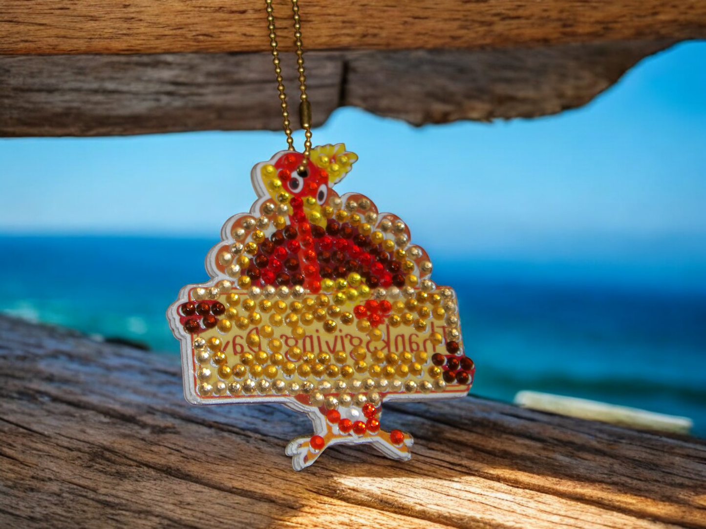 Turkey Thanksgiving Sign keychain decorated with colorful beads hanging on a wooden surface with ocean background