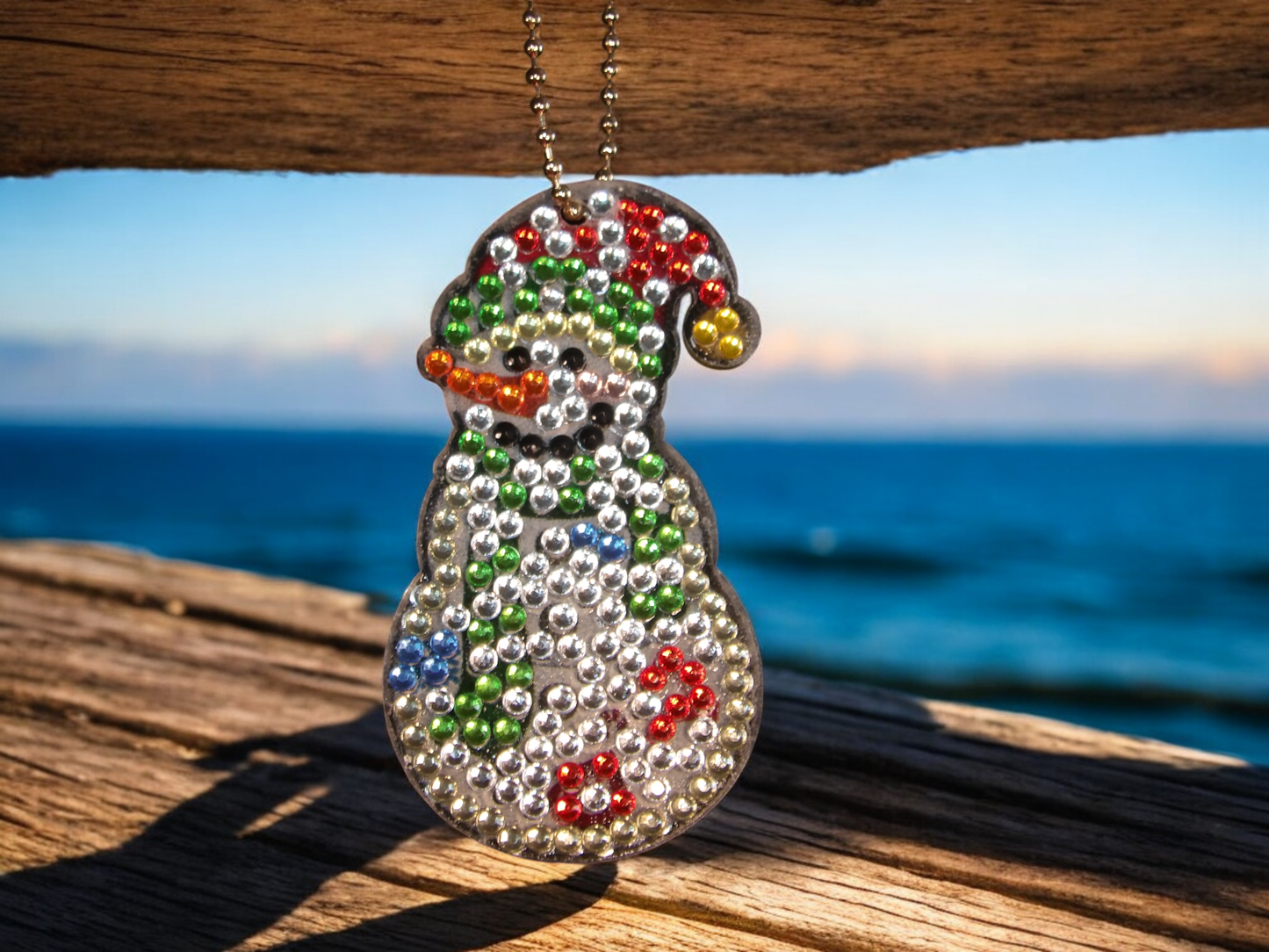 White fun snowman keychain with colorful beads hanging by the ocean and wooden surface background