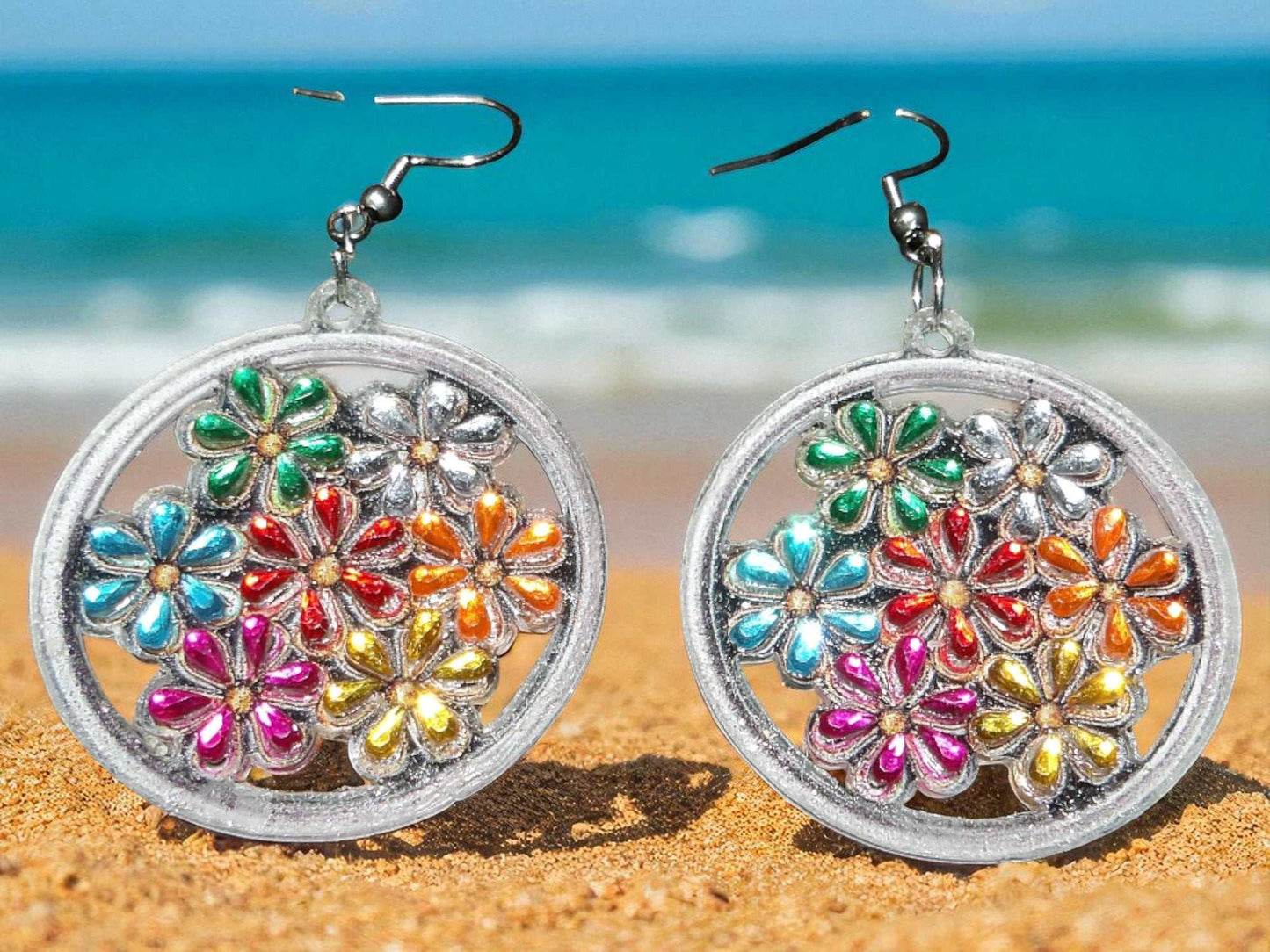 Colorful flowers earrings with vibrant handmade multicolor petals in silver circular frames on sandy beach background