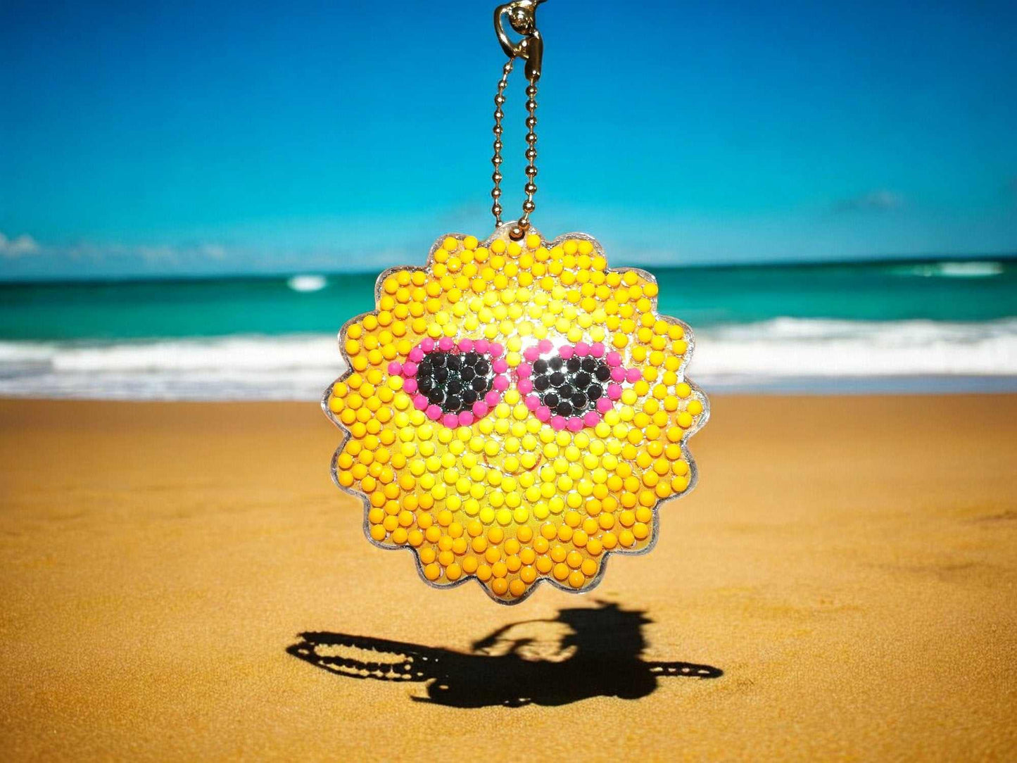 Sun with sunglasses keychain hanging on beach background