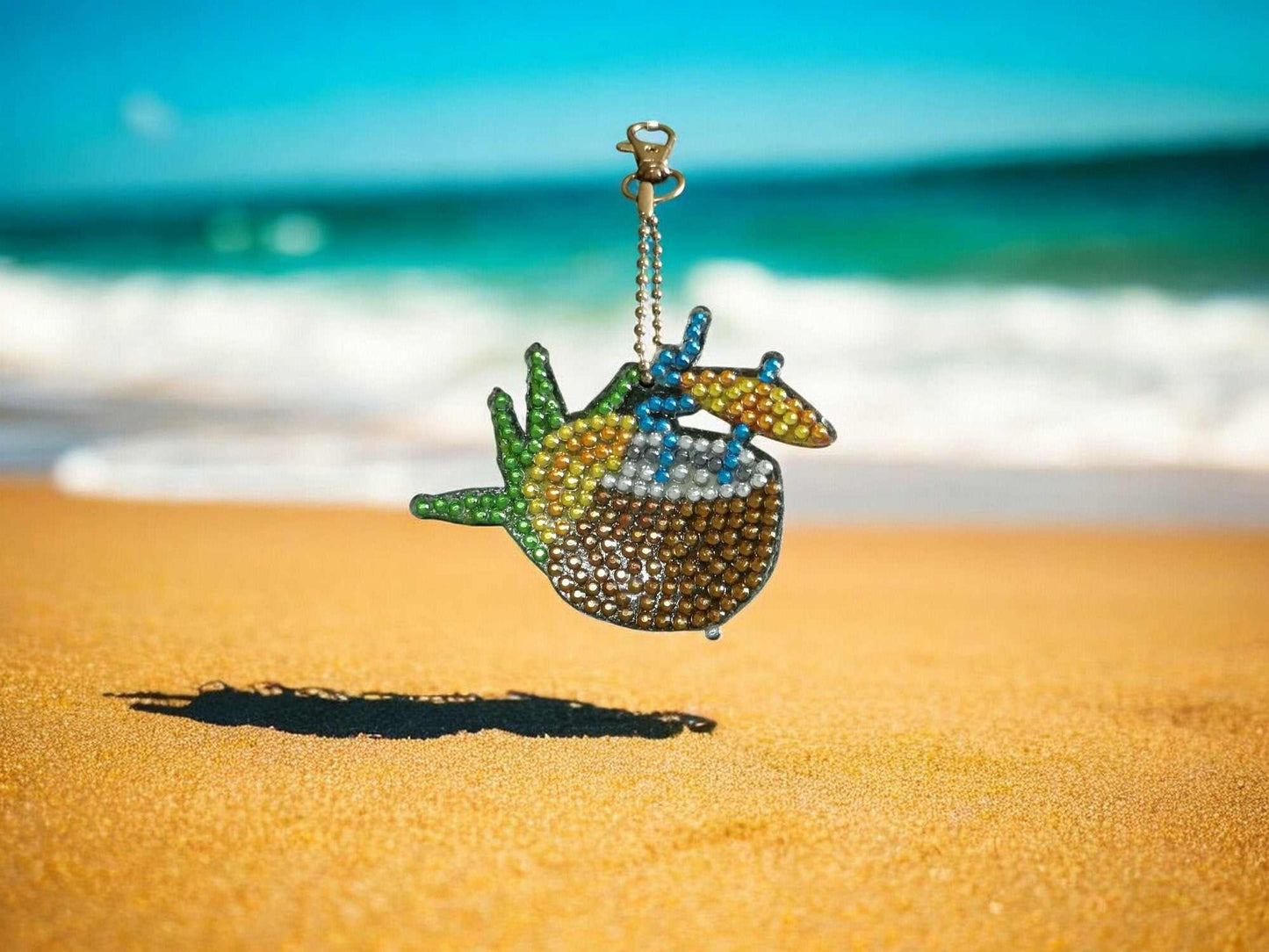 Summer drink with umbrella rhinestone keychain on sandy beach background