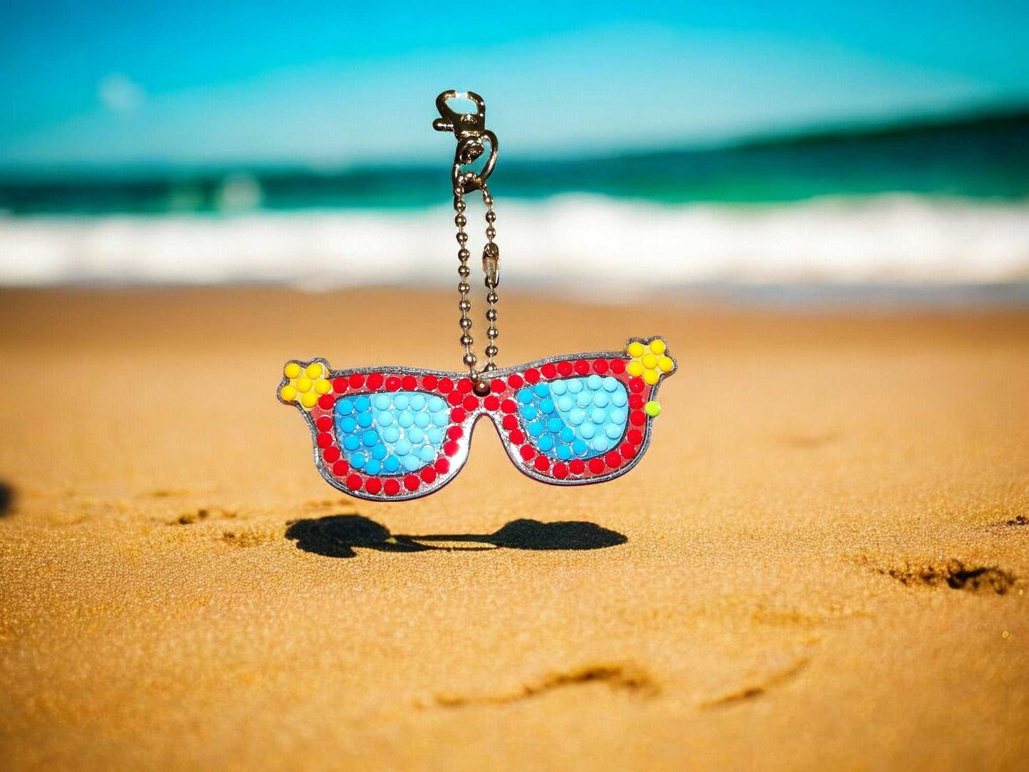 Colorful sunglasses keychain with blue lenses and red frame on beach sand