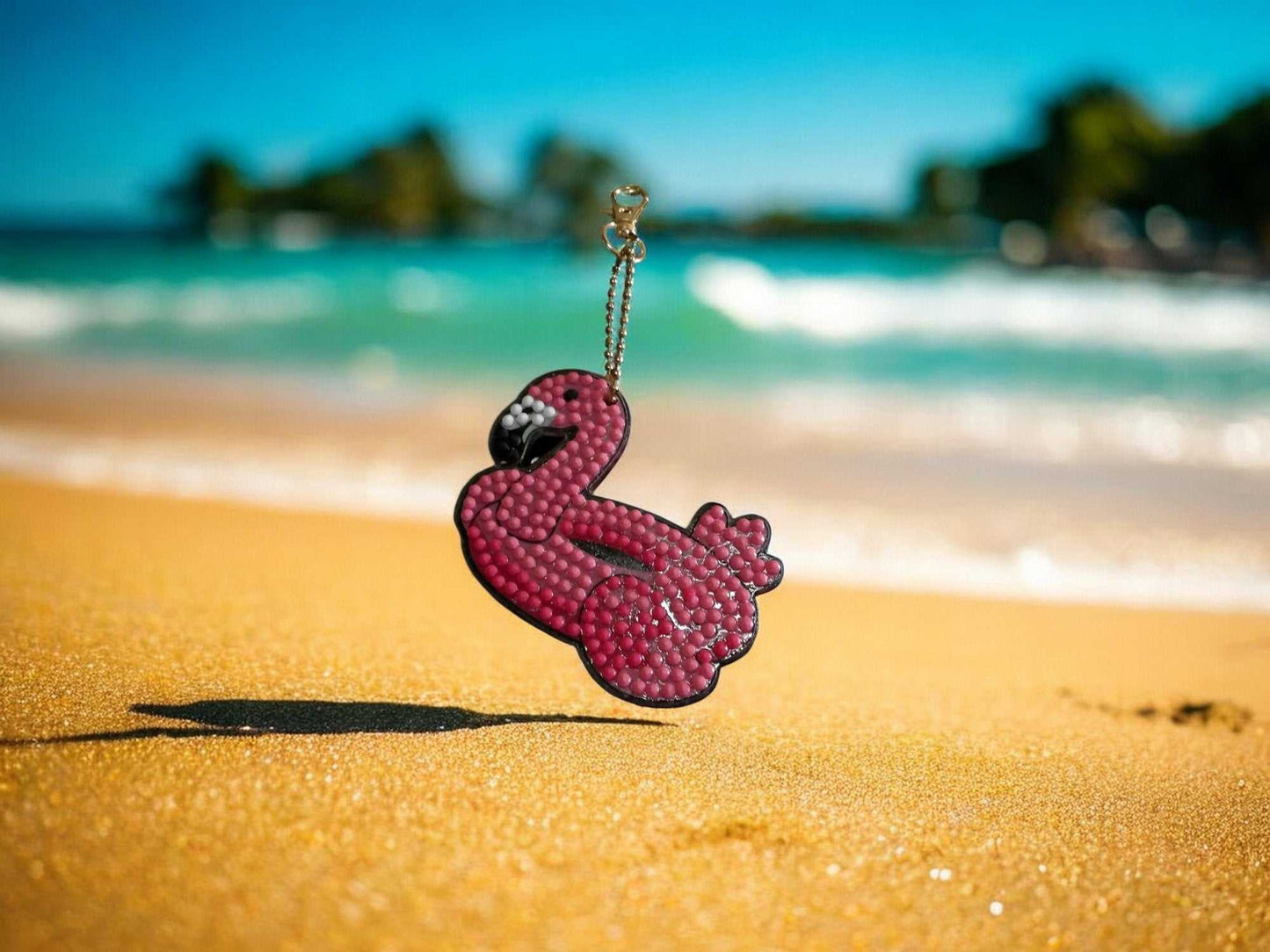 Pink Flamingo Beach Float Keychain on sandy beach background with ocean waves