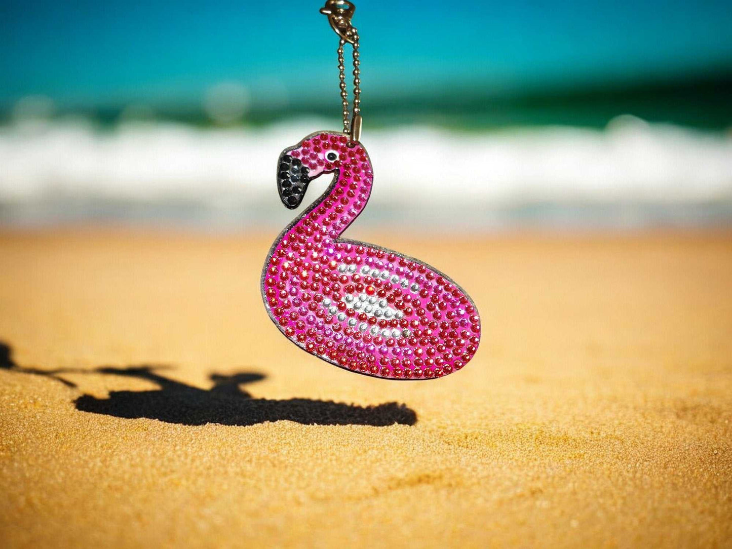 Pink flamingo float keychain adorned with rhinestones on sandy beach background
