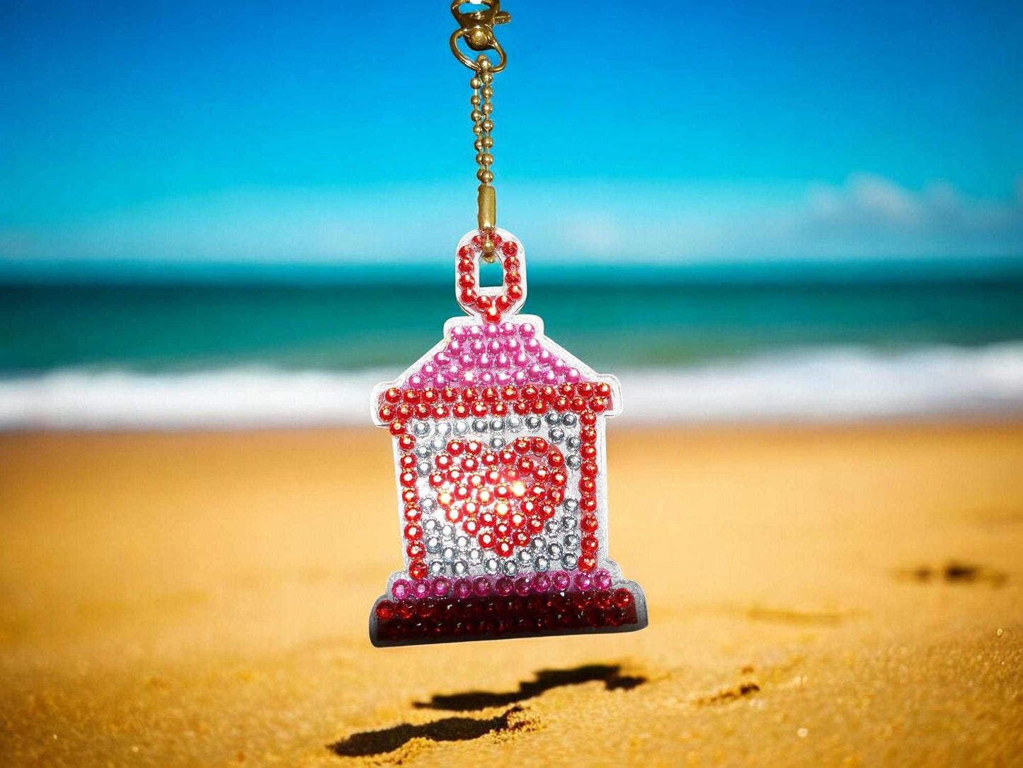 Red Heart Lantern Keychain with sparkling beads hanging on gold chain at beach background