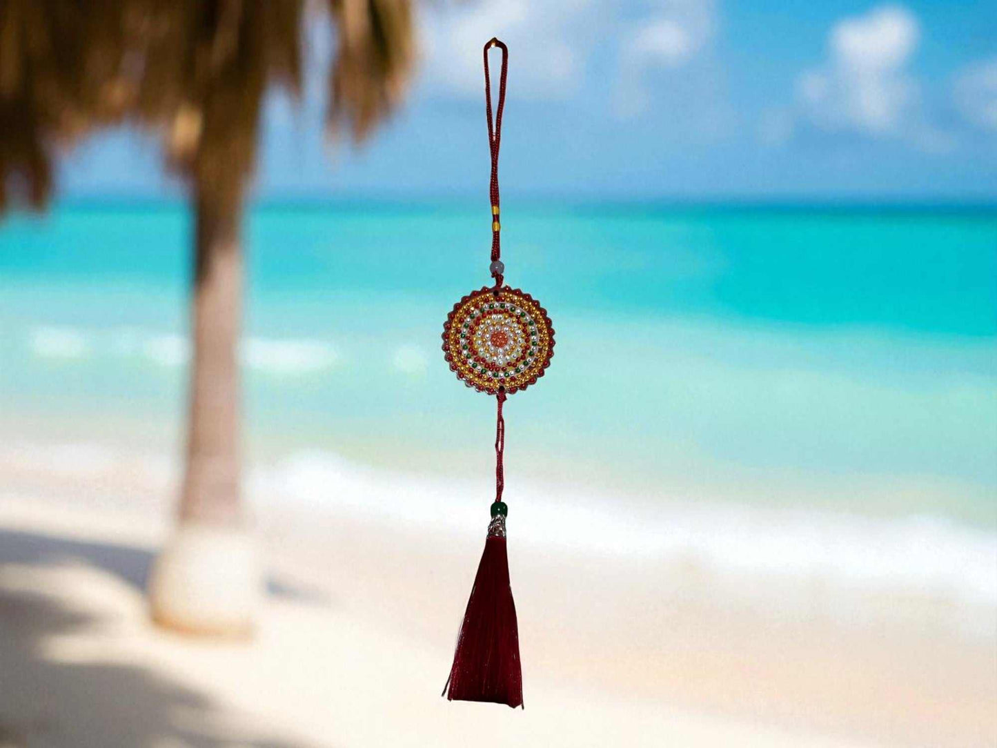Deep red colorful design car ornament with tassel hanging against beach background