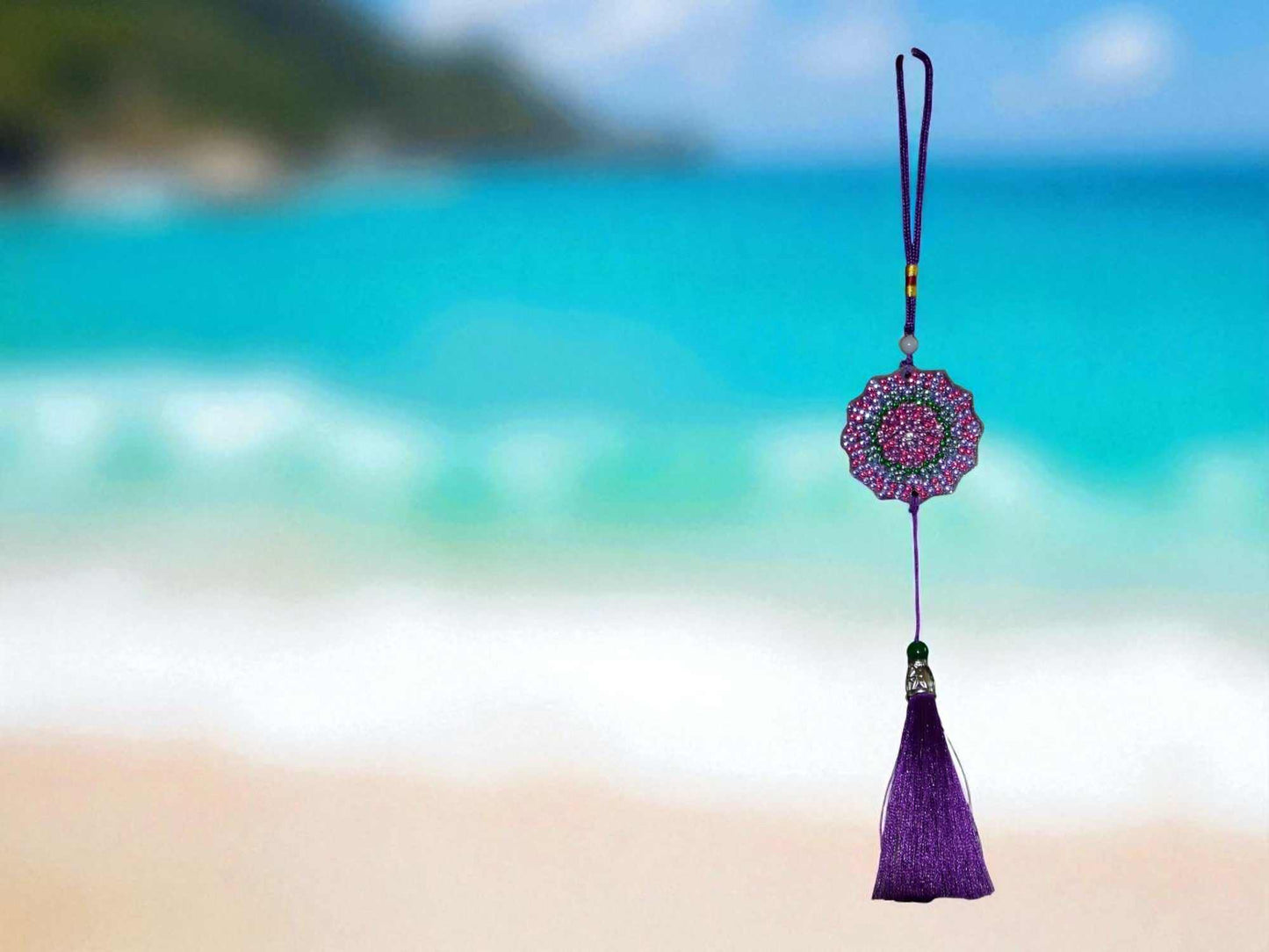 Deep Blue Colorful Design car ornament with vibrant purple tassel hanging against a blurred ocean background