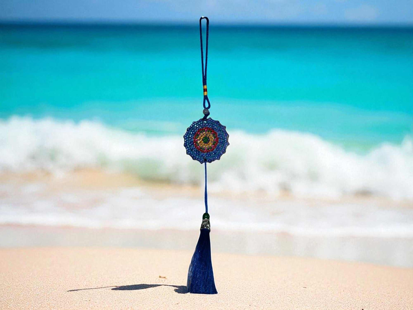 Dark blue colorful design car ornament with tassel hanging against beach background