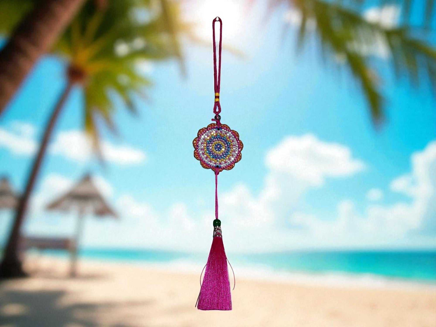 Pink colorful car ornament with tassel hanging against beach background