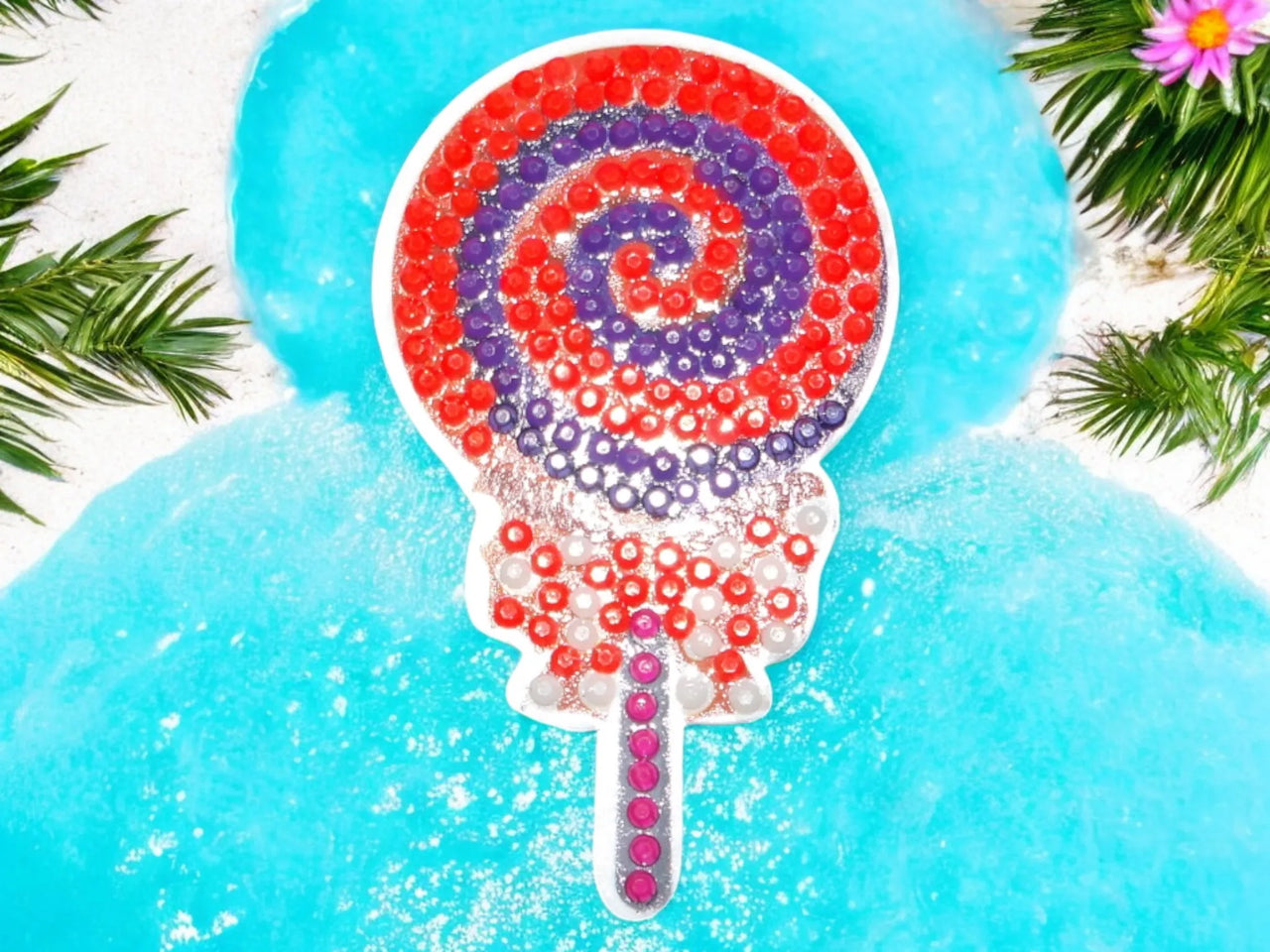 Glow in the dark colorful swirly lollipop magnet on blue background with greenery accents