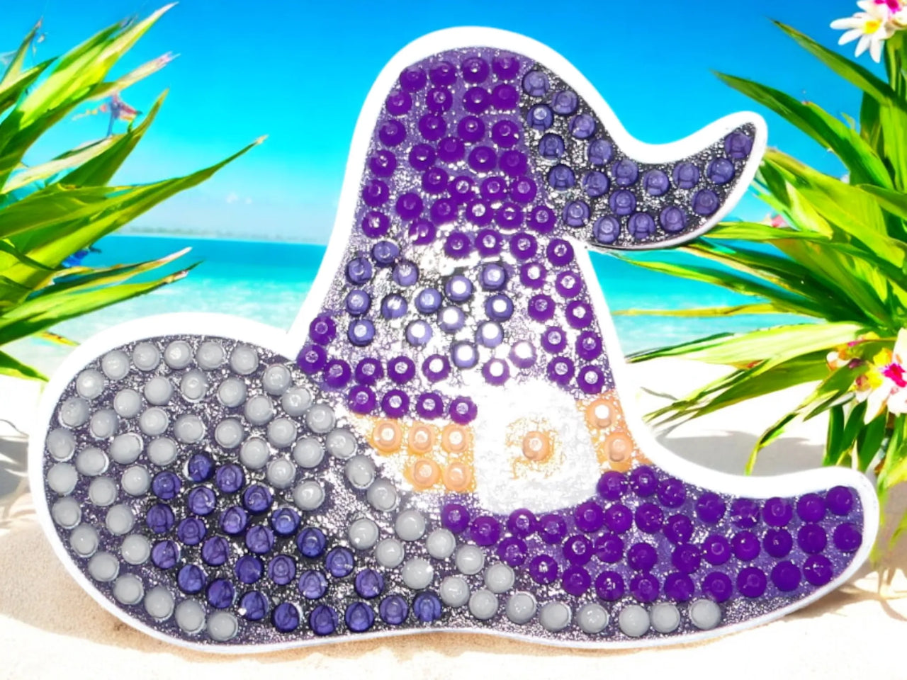 Glow in the dark purple-blue witches hat magnet with sparkling details on beach background