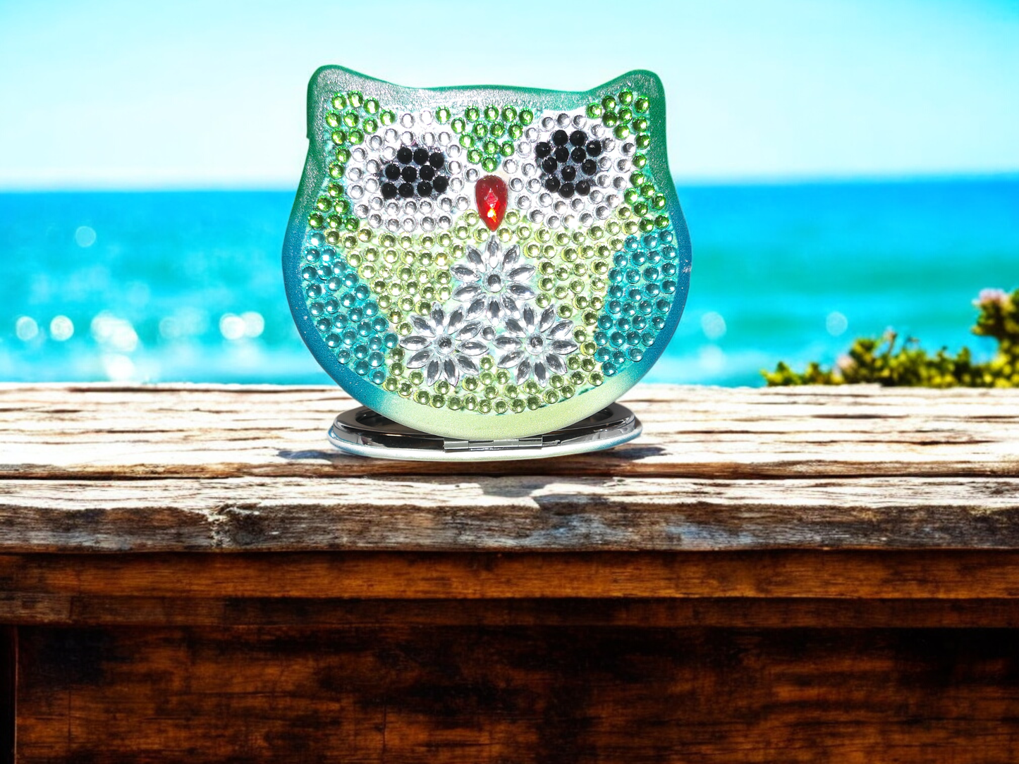 BlueGreen Owl Pocket Mirror with magnification and regular mirror sides decorated with blue and green rhinestones on wooden surface by the sea