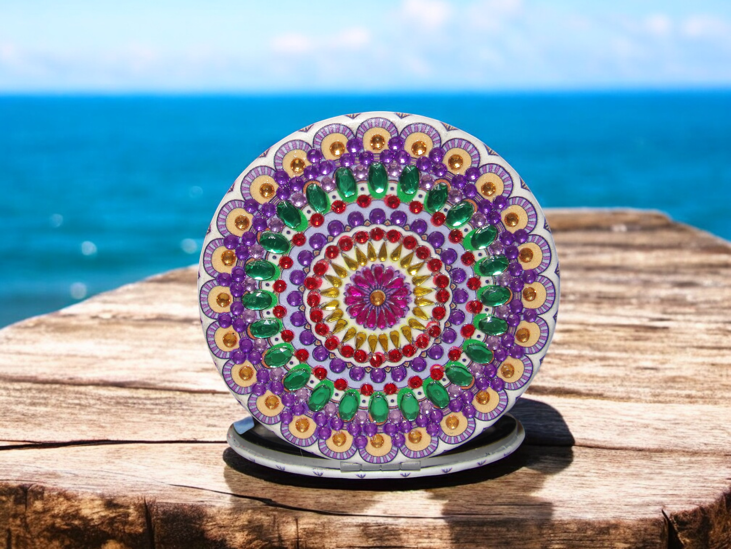 Round colorful pocket mirror with mandala design on wooden surface by the sea