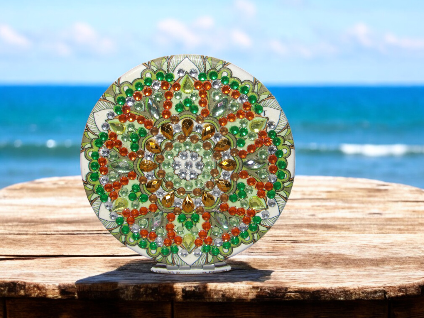 Green round pocket mirror with colorful mandala design and magnification feature on wooden surface by the sea