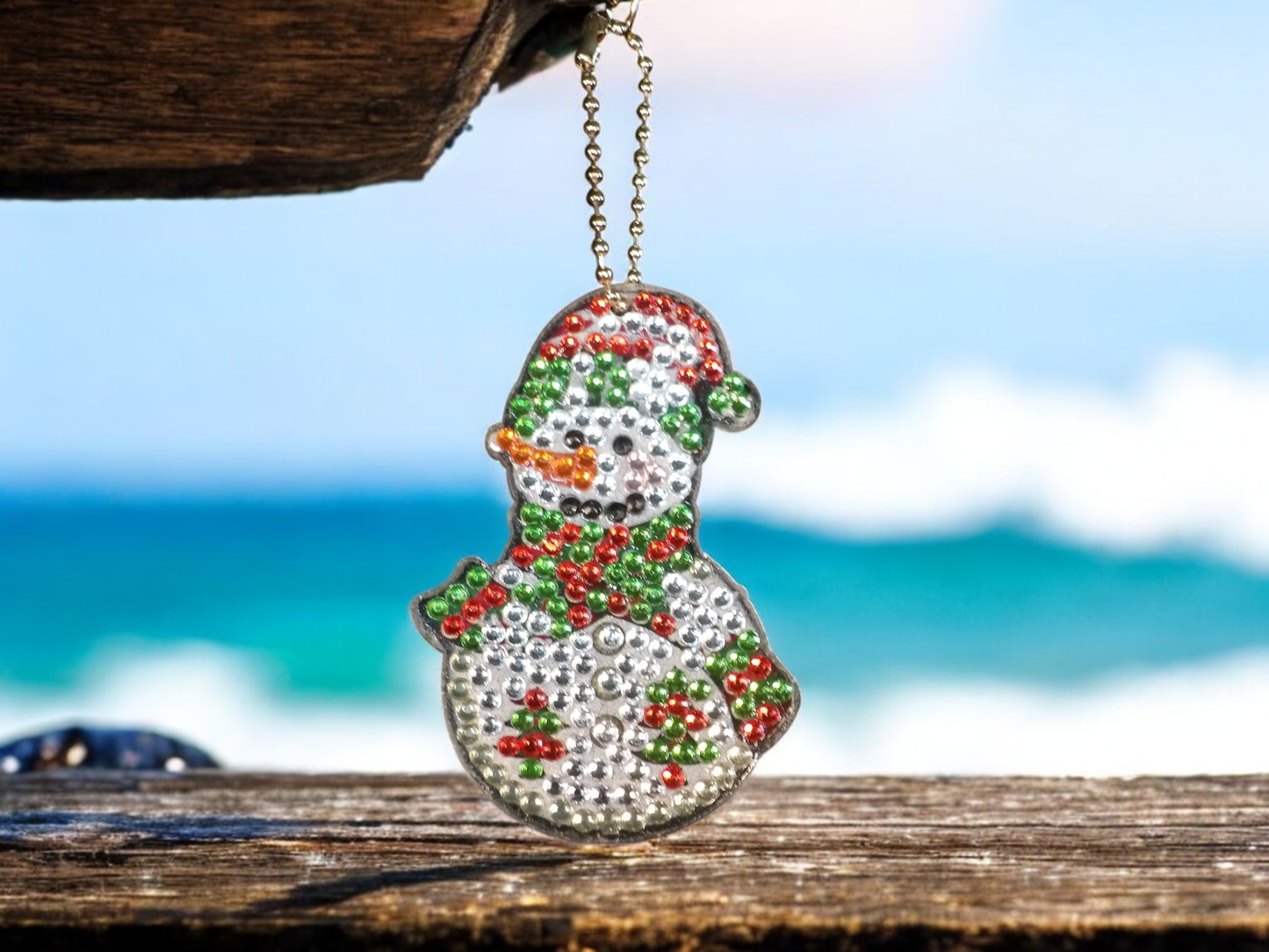 Green Tip Hat Snowman Keychain hanging with beach background