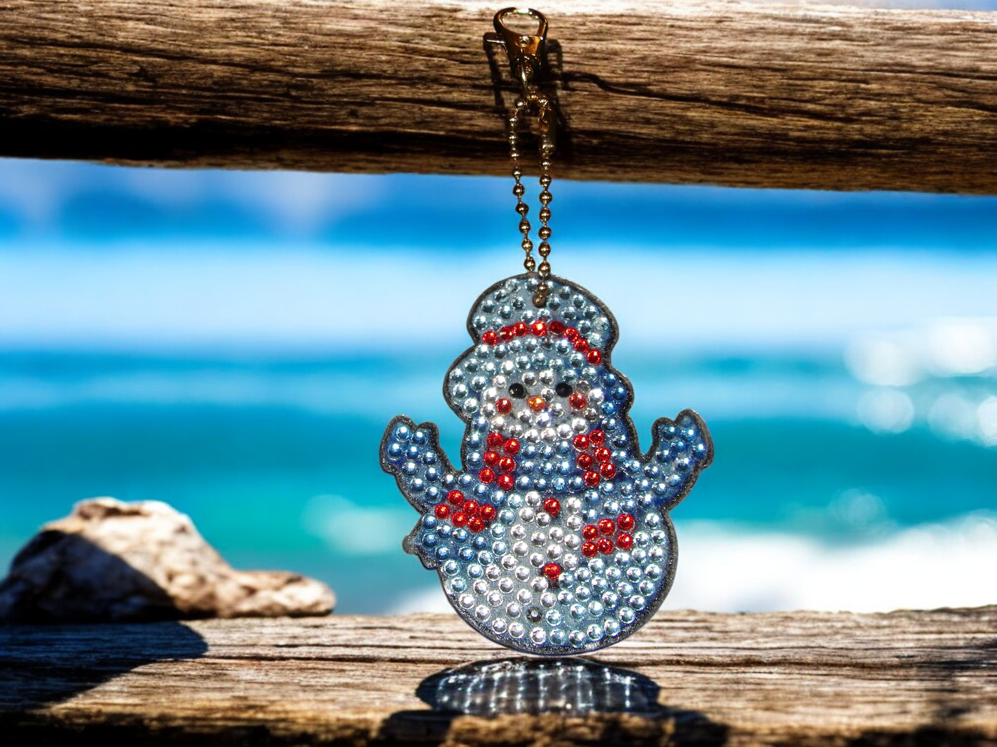 Keeping Warm Snowman Keychain with sparkling rhinestones hanging on wooden beam against blue sea background
