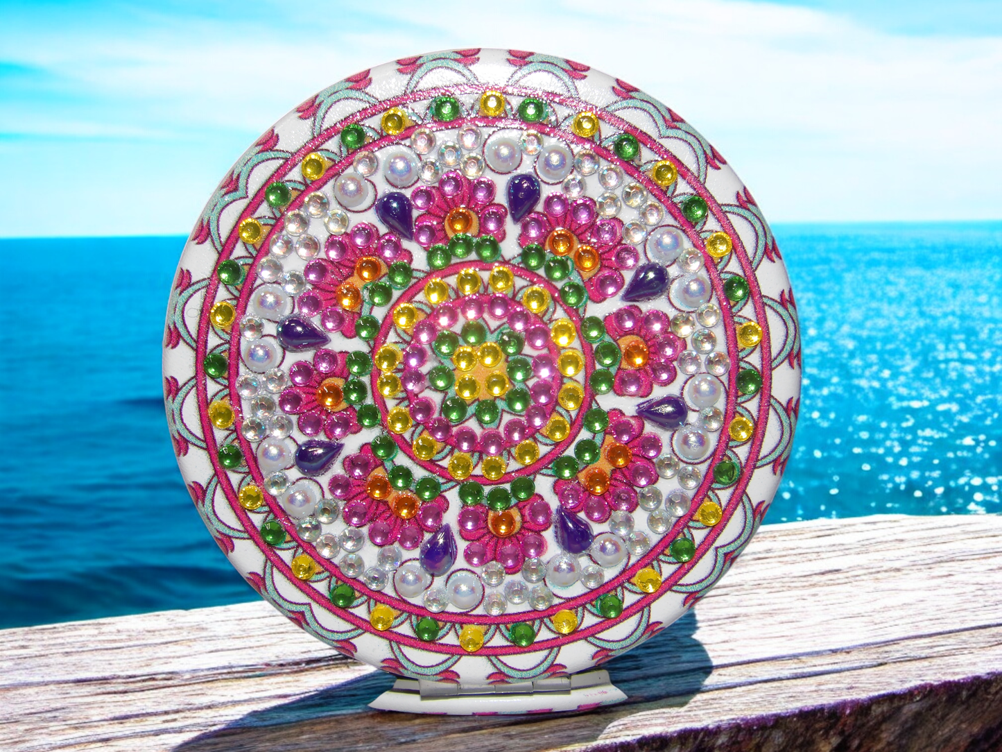 Round colorful mandala design pocket mirror with magnification and regular sides on wooden surface by the sea