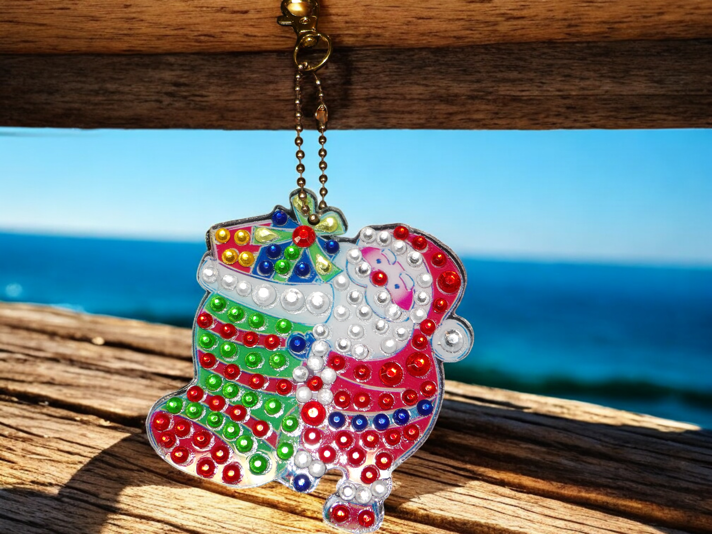 Colorful Santa Clause keychain with presents hanging on a wooden surface by the ocean