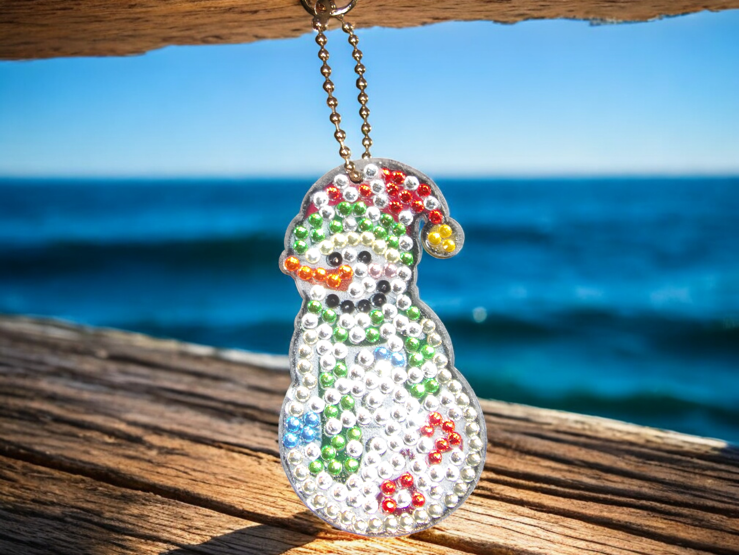 White fun snowman keychain with colorful rhinestones hanging outdoors near the ocean