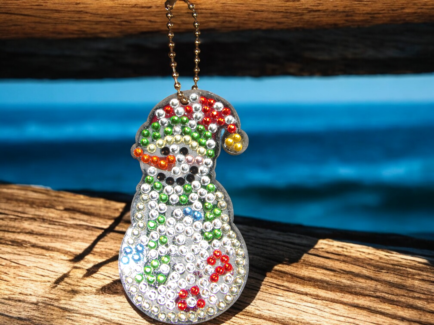 White Fun Snowman Keychain decorated with colorful rhinestones hanging on a wooden surface
