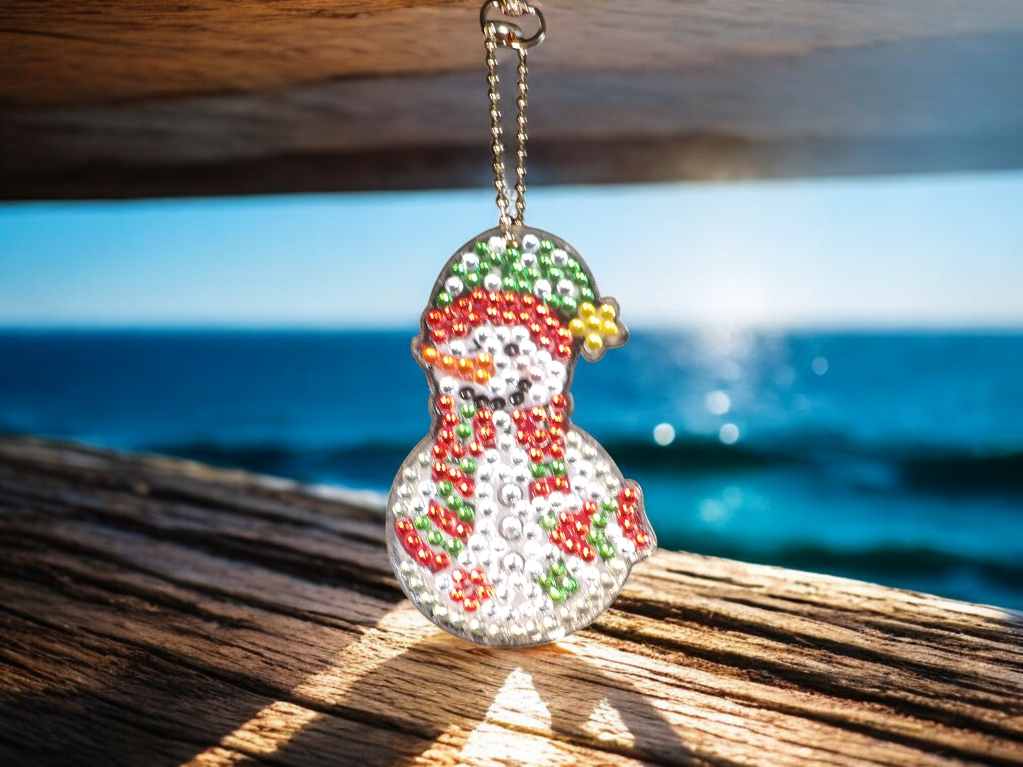 Yellow Tip Hat Snowman Keychain hanging by a wooden surface with ocean background