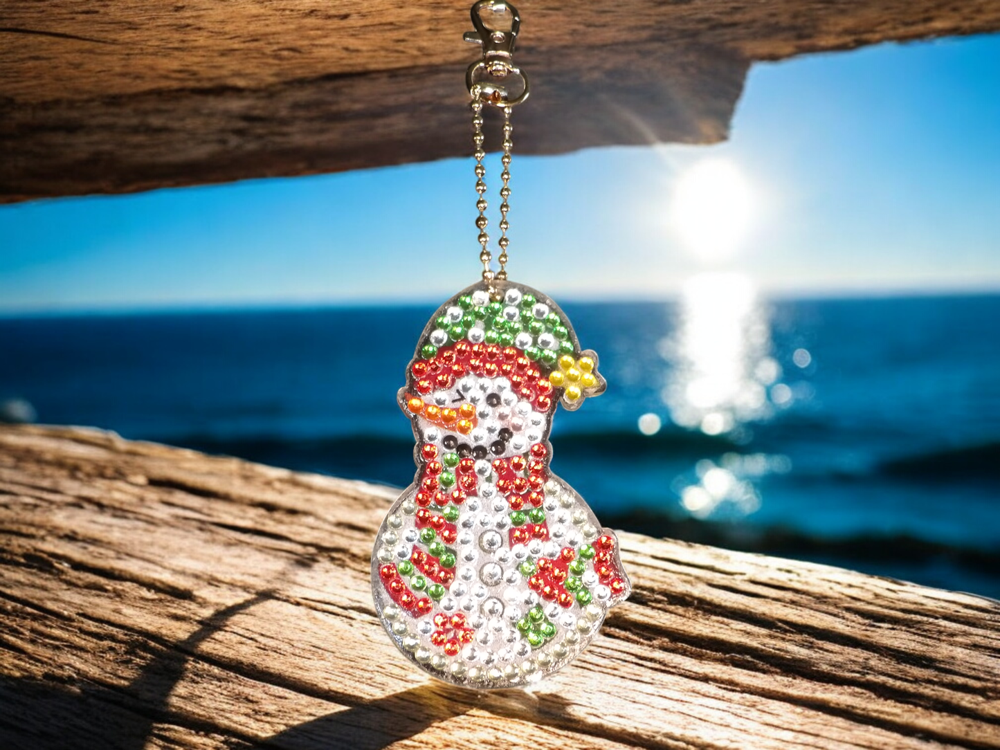 Yellow Tip Hat Snowman Keychain with colorful rhinestones hanging on a wooden surface by the sea
